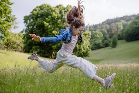 Foto de Retrato de una hermosa joven saltando en la hierba alta, divirtiéndose, disfrutando de un cálido día de primavera. - Imagen libre de derechos