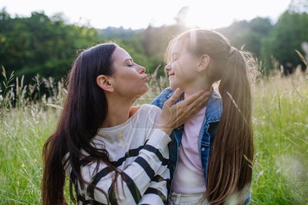 Photo for Beautiful mother with daughter, looking at each other while sitting in the grass at meadow. Concept of Mothers Day and maternal love. - Royalty Free Image