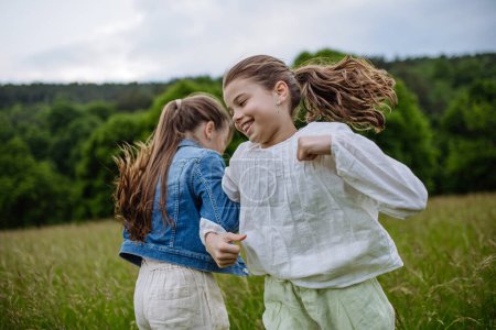 Photo for Two sisters playing at meadow in tall grass, running and dancing, having fun. Sisterly love and siblings relationship concept. - Royalty Free Image