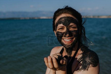 La mujer aplica barro sanador a su rostro y cuerpo. Barro curativo natural en Croacia en la playa. Lodo terapéutico o peloides ricos en minerales y sustancias orgánicas.