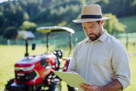 Téléchargez les photos : Un fermier lisant un document devant un tracteur sur le terrain. Subventions, prêts, possibilités de financement pour les agriculteurs. Soutien agricole, subventions. - en image libre de droit