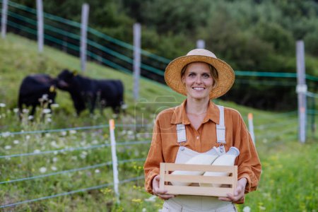 Portrait of female farmer holding harvest crate full of fresh vegetables, in front of paddock. Concept of multigenerational and family farming.