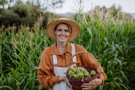 Téléchargez les photos : Portrait d'une agricultrice détenant un panier rempli de maïs récolté. Concept d'agriculture multigénérationnelle et familiale. - en image libre de droit