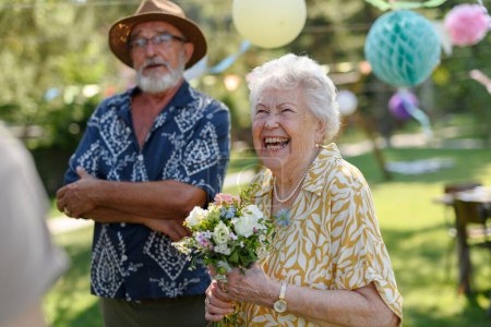 Photo for Garden birthday party for senior lady. Beautiful senior birthday woman receiving flowers as gift. - Royalty Free Image