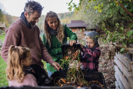 Family removing compost from a composter in garden, and also composting kitchen waste in composter. Concept of composting and sustainable organic gardening.