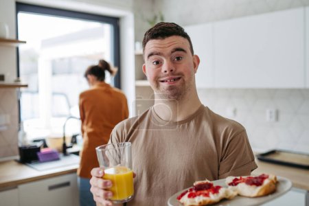 Young man with Down syndrome holding breakfast and glass of juice. Morning routine for man with Down syndrome genetic disorder.