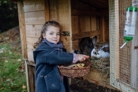 Téléchargez les photos : La fille nourrit le lapin animal, lui donnant des légumes du jardin et du vieux pain. - en image libre de droit