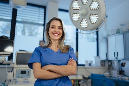 Photo for Portrait of ER doctor in hospital working in emergency room. Portrait of the beautiful nurse in blue uniform, crossed arms, smiling. - Royalty Free Image