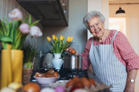 Photo for Senior woman preparing traditional easter meals for family, boiling eggs. Recreating family traditions and customs. Concept of easter holidays and traditions. - Royalty Free Image