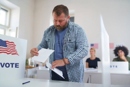 Électeur masculin remplissant le bulletin de vote, mettant son vote dans l'urne. Citoyen américain votant dans un bureau de vote le jour du scrutin, élections américaines.