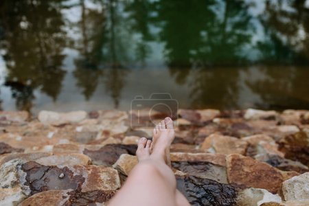 Téléchargez les photos : Vue du dessus des jambes de la jeune femme sur des escaliers en pierre dans un étang naturel pendant les vacances d'été en montagne. - en image libre de droit