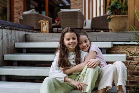 Photo for Two sisters sitting on front porch stairs in front of house, embracing. Sisterly love and siblings relationship concept. - Royalty Free Image