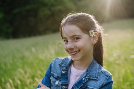 Photo for Portrait of beautiful young girl with flower behind the ear, standing on meadow, enjoying warm spring day. - Royalty Free Image
