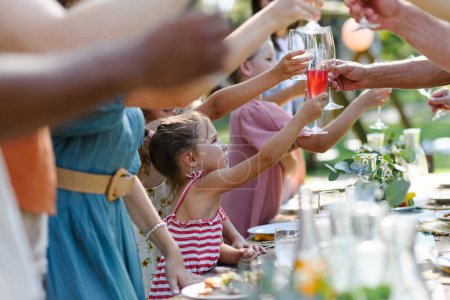 Photo for Family clinking glasses at summer garden party, kids clinking with nonalcoholic drink, lemonade. Celebratory toast at the table. Big family garden bbq. - Royalty Free Image