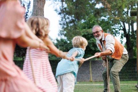 Photo for Grandfather has tug of war with their grandchildren. Fun games at family garden party. - Royalty Free Image