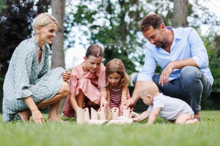Familia jugando en la hierba con juego de jardín de madera. Padre, madre y tres niños se divierten en la fiesta de cumpleaños.