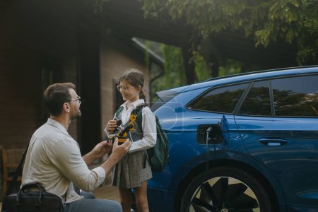 Father handing girl her science project, robotic arm for school science fair. Electric car is charging before going to school and work. Concept of young girls in science.