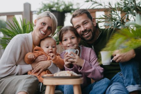 Photo for Portrait of family sitting outdoors in the garden patio. Drinking warm tea and eating sweet roll bread. Hygge family autumn time. - Royalty Free Image