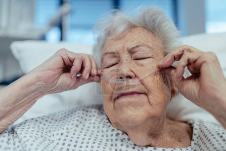 Porträt einer Seniorin nach Schlaganfall, erholendem Herzinfarkt, liegend im Krankenhausbett. Älterer Patient im Krankenhauskittel mit Nasenkanüle.