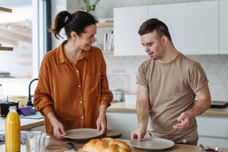 Photo for Young man with Down syndrome preparing breakfast with his mother at home. Morning routine for man with Down syndrome genetic disorder. - Royalty Free Image