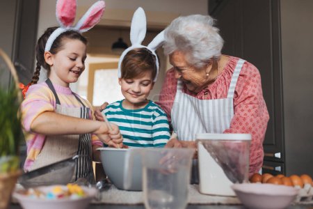 Großmutter mit Enkeln bereitet traditionelle Osterspeisen zu, backt Kuchen und Süßigkeiten. Die Weitergabe von Familienrezepten, Brauchtum und Geschichten. Konzept für Familien-Osterferien.