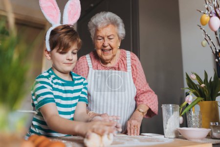 Großmutter mit Enkel bereitet traditionelle Osterspeisen zu, knetet Teig für Osterbrötchen. Die Weitergabe von Familienrezepten, Brauchtum und Geschichten. Konzept für Familien-Osterferien.