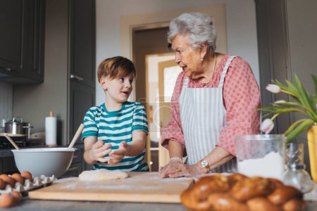 Großmutter mit Enkel bereitet traditionelle Osterspeisen zu, knetet Teig für Osterbrötchen. Die Weitergabe von Familienrezepten, Brauchtum und Geschichten. Konzept für Familien-Osterferien.