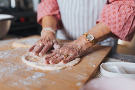 Großaufnahme der Hände einer Seniorin, die traditionelle Ostermahlzeiten für die Familie zubereitet, Teig für Osterbrötchen knetet. Nachmachen von Familienrezepten, Brauch. Konzept der Osterfeiertage und Traditionen.