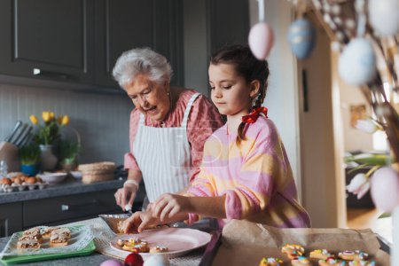 Photo for Grandmother with granddaughter preparing traditional easter meals, baking cakes and sweets. Passing down family recipes, custom and stories. Concept of family easter holidays. - Royalty Free Image