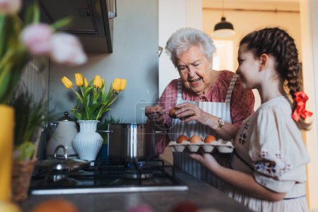 Großmutter mit Enkelin bereitet traditionelle Osterspeisen zu, kocht Eier mit natürlichem Farbstoff, um Schalen zu färben. Die Weitergabe von Familienrezepten, Brauchtum und Geschichten. Konzept für Familien-Osterferien.