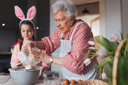 Großmutter mit Enkelin bereitet traditionelle Osterspeisen zu, backt Kuchen und Süßigkeiten. Die Weitergabe von Familienrezepten, Brauchtum und Geschichten. Konzept für Familien-Osterferien.