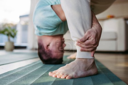 Young man with Down syndrome exercising at home, stretching his body, legs. Workout routine for disabled man.