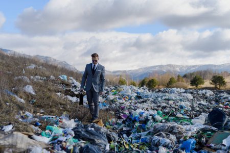 Photo for Fashionable businessman walking across on landfill, large pile of waste. Consumerism versus pollution concept. Corporate social responsiblity in business. - Royalty Free Image