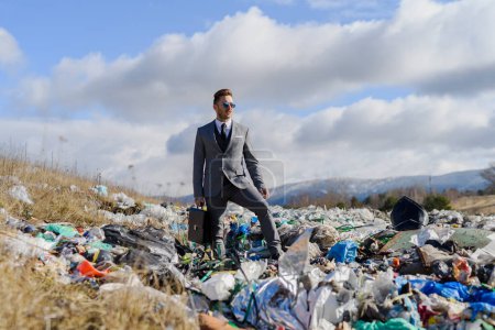 Photo for Fashionable modern businessman standing on landfill, large pile of waste. Consumerism versus pollution concept. Corporate social responsiblity in business. - Royalty Free Image