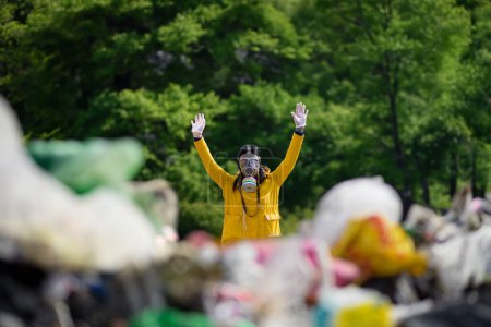 Foto de Activista femenina con máscara de gas cogida de la mano, parada en vertedero, gran pila de residuos, concepto ambiental y activismo ecológico. - Imagen libre de derechos
