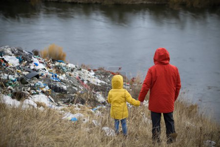 Foto de Niña entre eco activistas recogiendo basura a lo largo de la orilla del río, en la naturaleza, la contaminación ambiental, el activismo ecológico y el concepto de plogging. - Imagen libre de derechos
