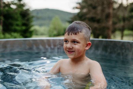 Foto de Little boy enjoying summer time in the outdoor pool with his family, having fun. - Imagen libre de derechos