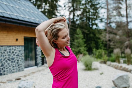 Photo for Young woman stretching before exercise, trail running in the forest, getting ready on a mountain cottage patio surrounded by nature. - Royalty Free Image