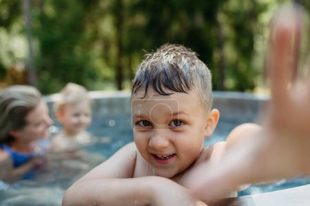 Téléchargez les photos : Little boy enjoying summer time in the outdoor pool with his family, having fun. - en image libre de droit