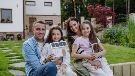 Photo for Happy family holding model of house with solar panels on roof and wind turbine model. Alternative, renewable, green energy and sustainable lifestyle concept. - Royalty Free Image