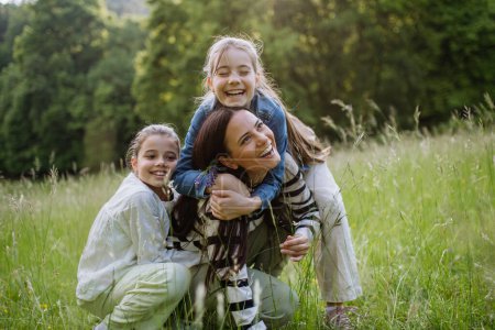 Photo for Beautiful mother with two daughters, embracing, laughing at meadow. Concept of Mothers Day and maternal love. - Royalty Free Image
