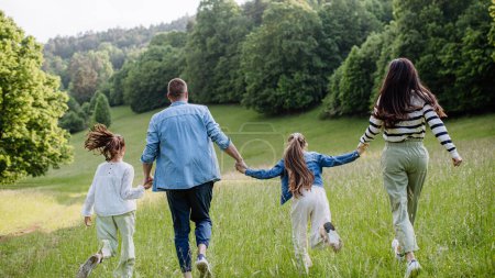 Foto de Vista trasera de la hermosa familia joven caminando, corriendo a través de la hierba en el prado, disfrutando juntos tiempo. - Imagen libre de derechos