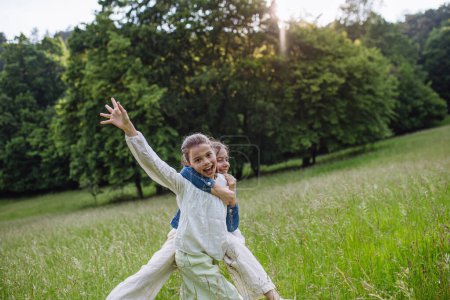 Two sisters playing at meadow in tall grass, having fun, running a laughing. Sisterly love and siblings relationship concept.
