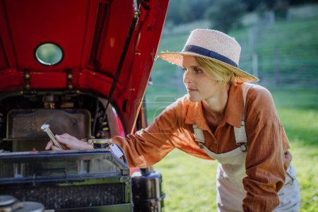 Bäuerin repariert Traktor, Traktorwartung. Progressive Bäuerin arbeitet auf ihrem eigenen Hof am Traktor. Frauen in der Landwirtschaft.