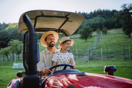Foto de Padre granjero montando tractor con su hija. Niña creciendo en una granja familiar. Concepto de agricultura multigeneracional. - Imagen libre de derechos