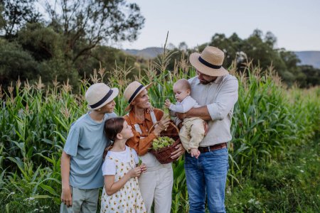 Téléchargez les photos : Une famille de fermiers debout devant un champ de maïs. Concept d'agriculture multigénérationnelle et familiale. - en image libre de droit