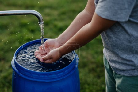 Téléchargez les photos : Garçon se lavant les mains avec de l'eau d'un puits. Eh bien avec une pompe pour le lavage extérieur dans le jardin. - en image libre de droit