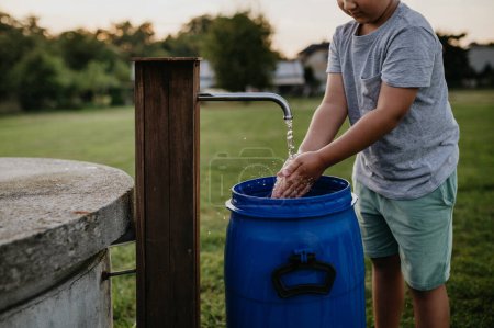 Photo for Boy washing his hands with water from a well. Well with a pump for outdoor washing in the garden. - Royalty Free Image