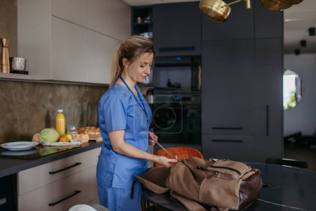 Photo for Female nurse, doctor getting ready for work, packing backpack, leaving house in scrubs with backpack. Work-life balance for healthcare worker. - Royalty Free Image