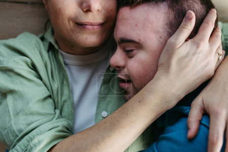 Téléchargez les photos : Portrait d'un jeune homme trisomique avec sa mère à la maison, tenant, touchant le front. Concept d'amour et parentalité enfant handicapé. Gros plan. - en image libre de droit